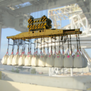 Large crane lifting multiple white bulk bags with chains at an industrial site.